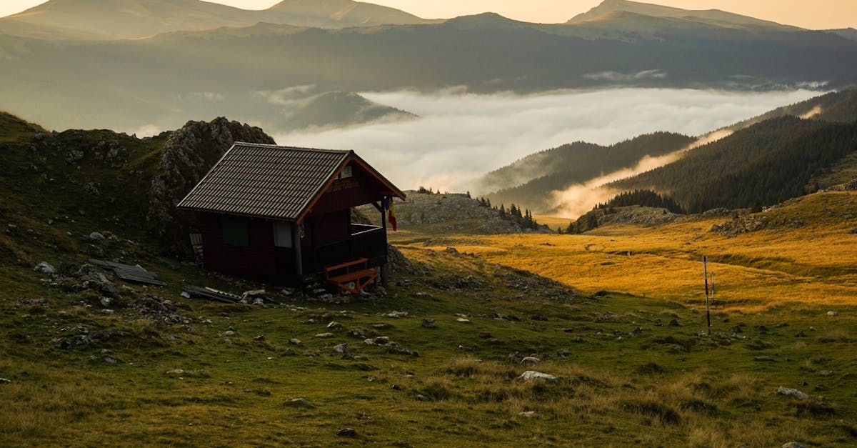 A small hut is sitting on top of a grassy hill in the mountains. High Country Outfitters