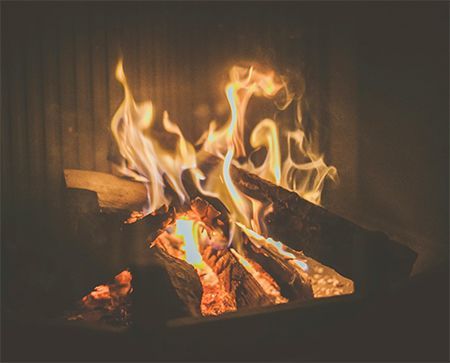 A tree in front of a house with a wooden deck and stairs. The house has gray siding and large windows.