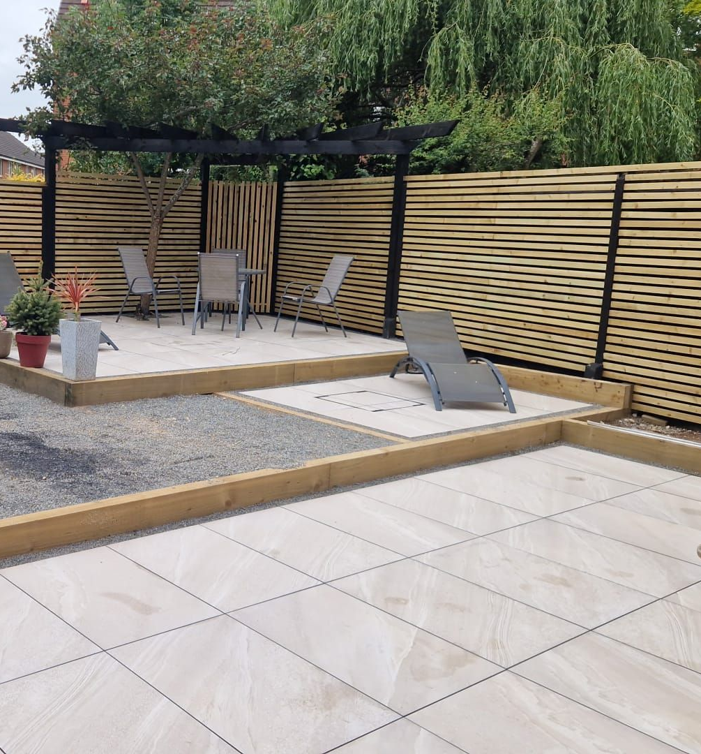 Patio with light pavers, wood slat fence, lounge chairs, and pergola.