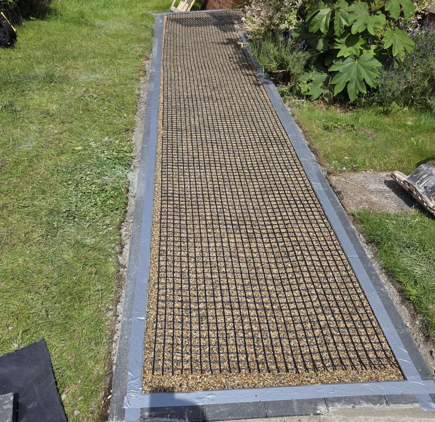 Pathway made with gravel and grid, bordered by metal on a grassy area.