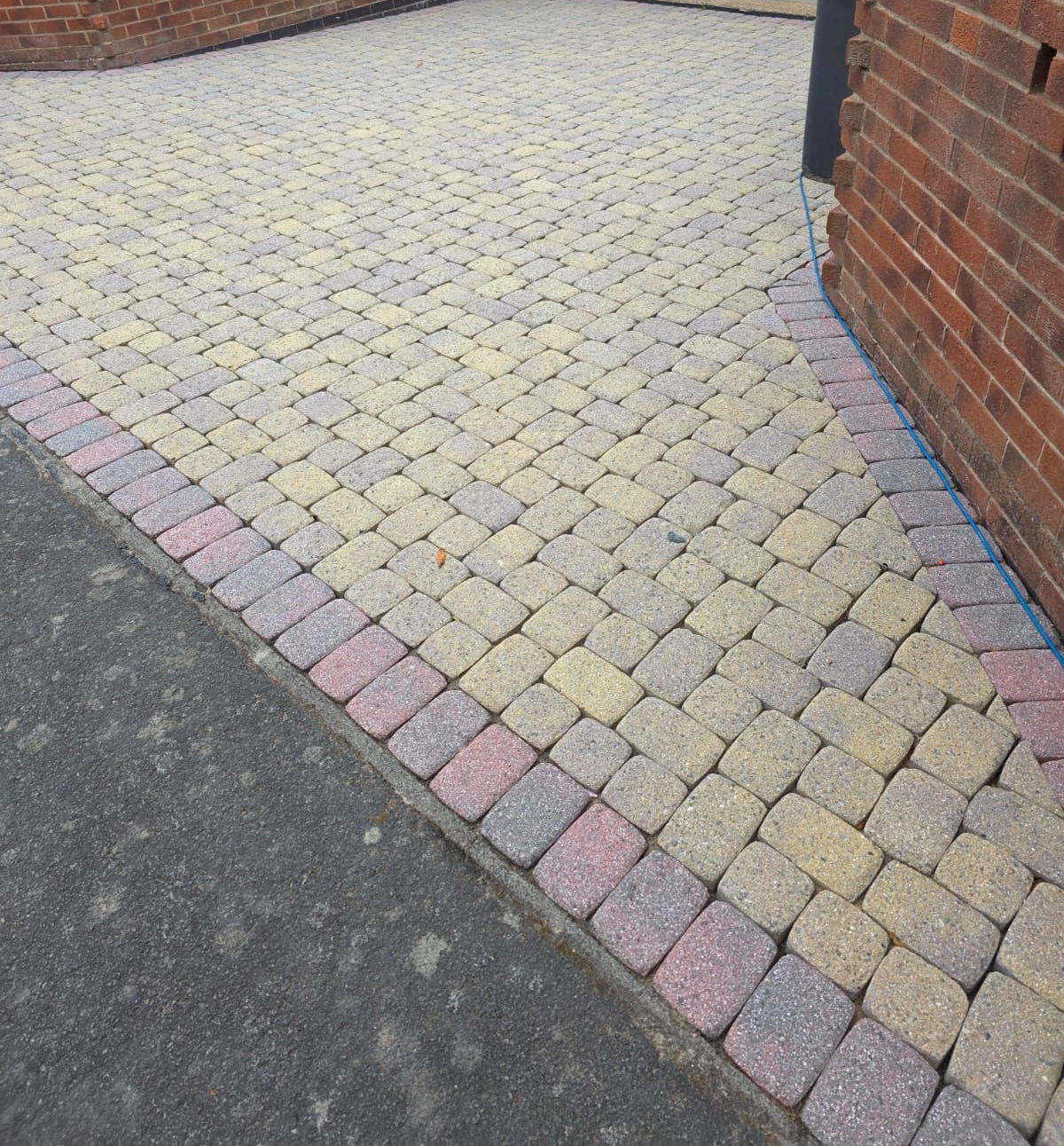 Brick paved walkway with a colored border next to a brick building.