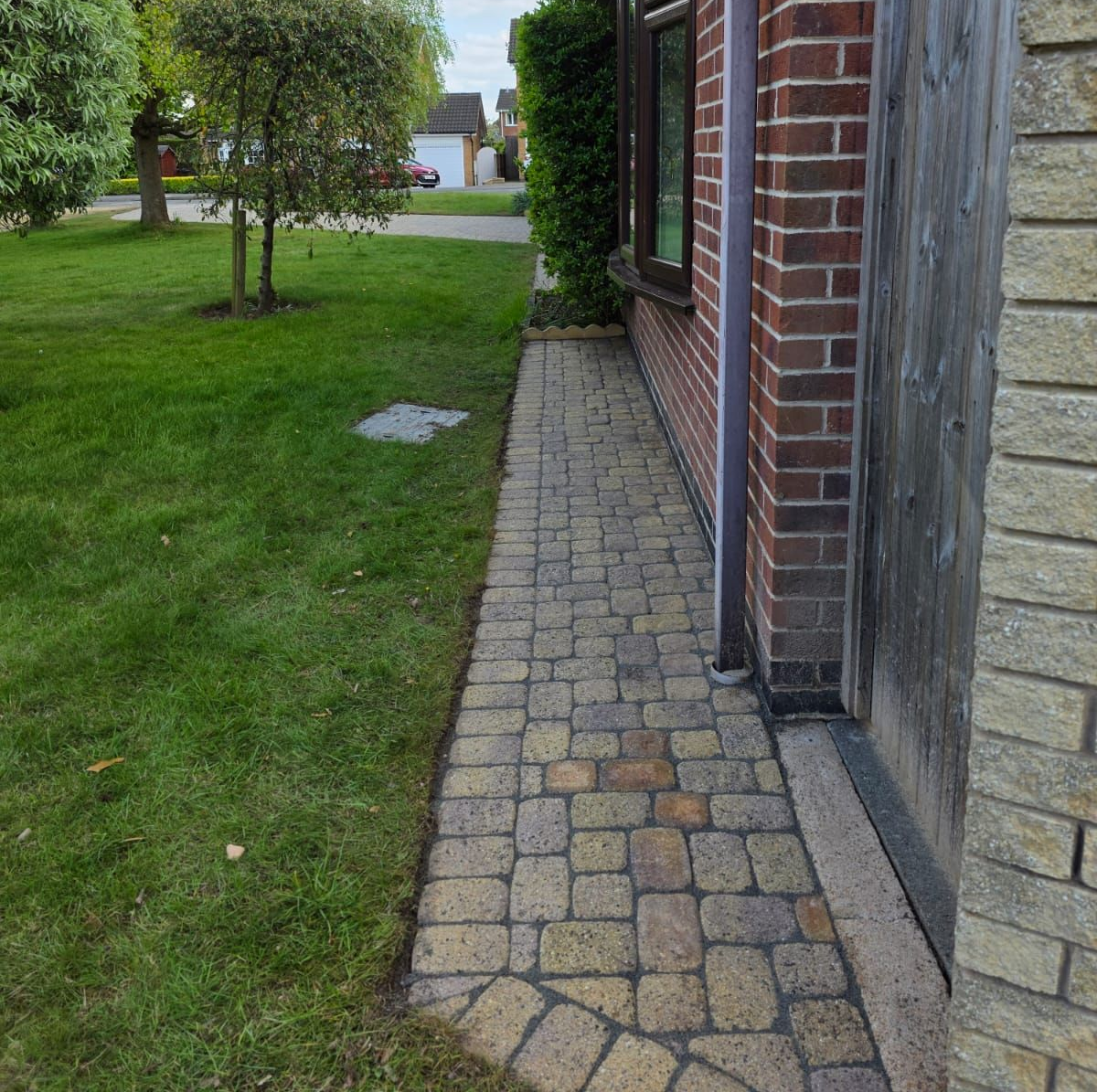 A brick path alongside a building's wall and a green lawn.