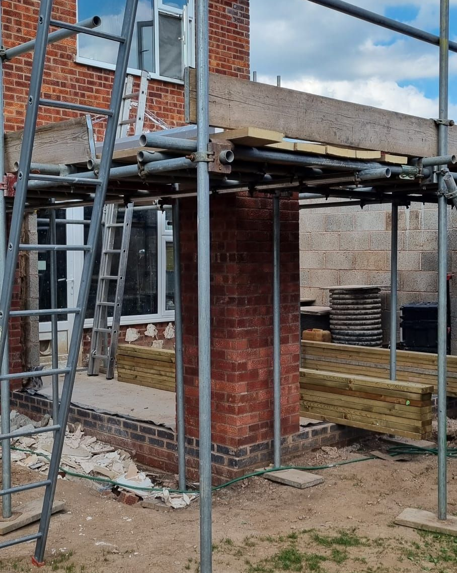 Brick structure under construction, with scaffolding around and wooden planks supporting the top.
