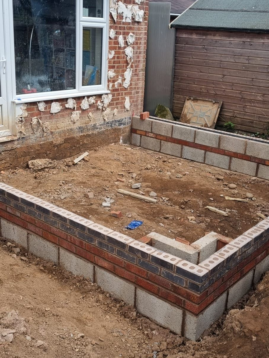 Construction site, foundation of a building with brick and cinder block walls. Earth fill is visible inside the foundation.