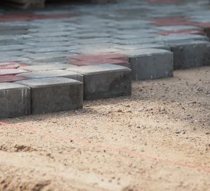 Gray paving stones being laid on a bed of sand, red stones interspersed.