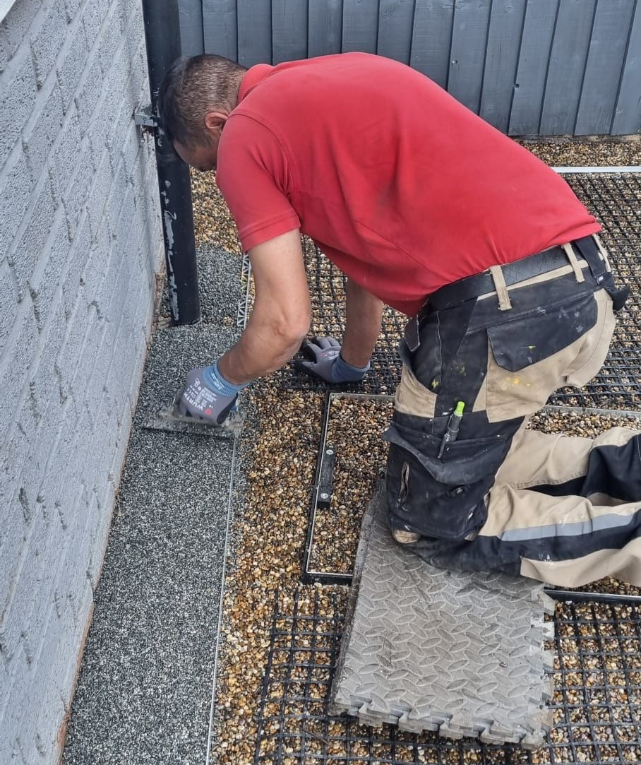 Man in red shirt laying paving stones on a surface, next to a wall.