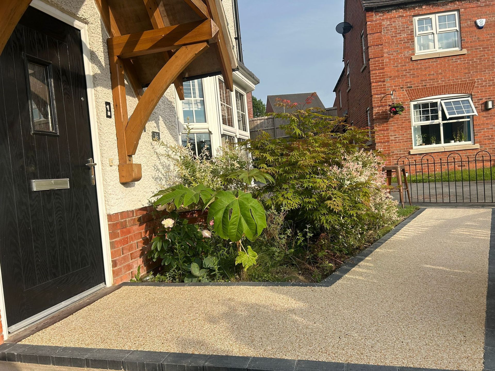 House entrance with black door, gravel path, and garden. A brick house is to the right - resin pathway