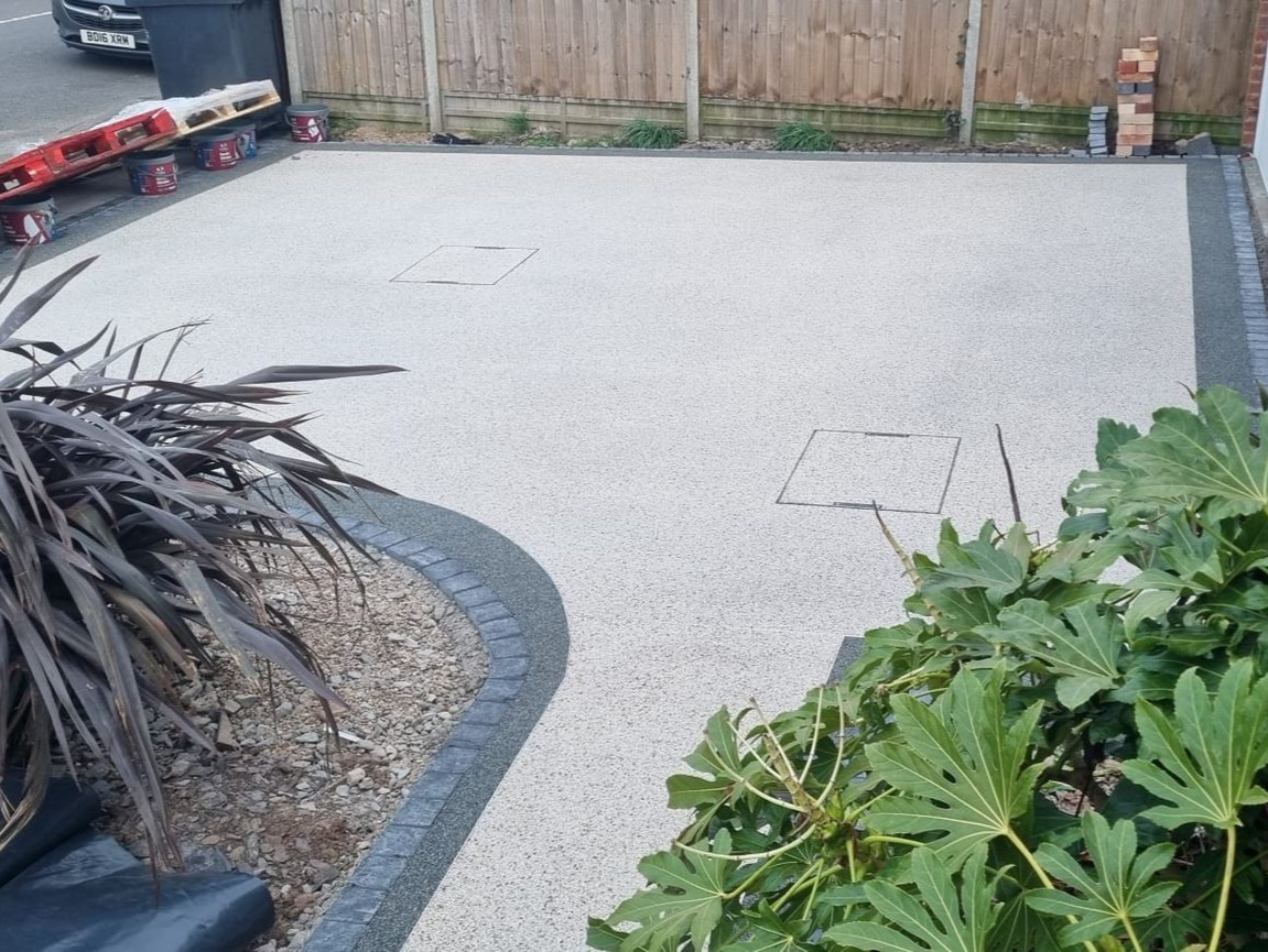 Gravel driveway with dark edging, bordered by a wooden fence and greenery - resin driveway