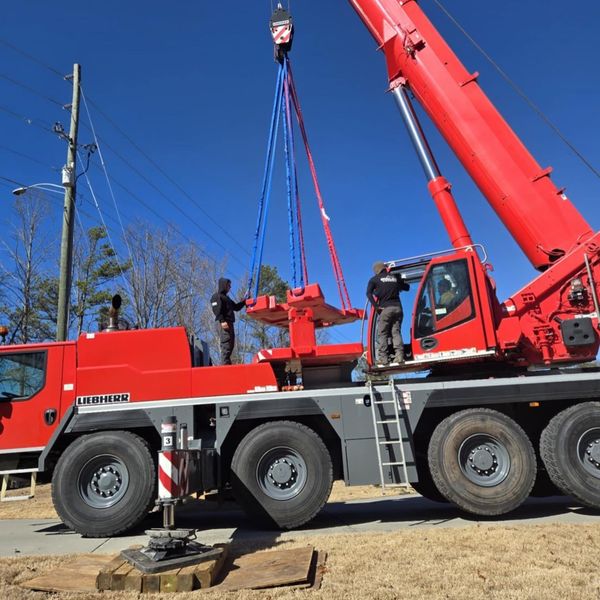 Red crane lifting a metal object. Two workers on the crane. Blue sky, sunny day.