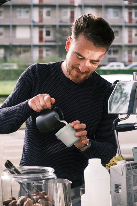 Een man giet melk in een kopje koffie.