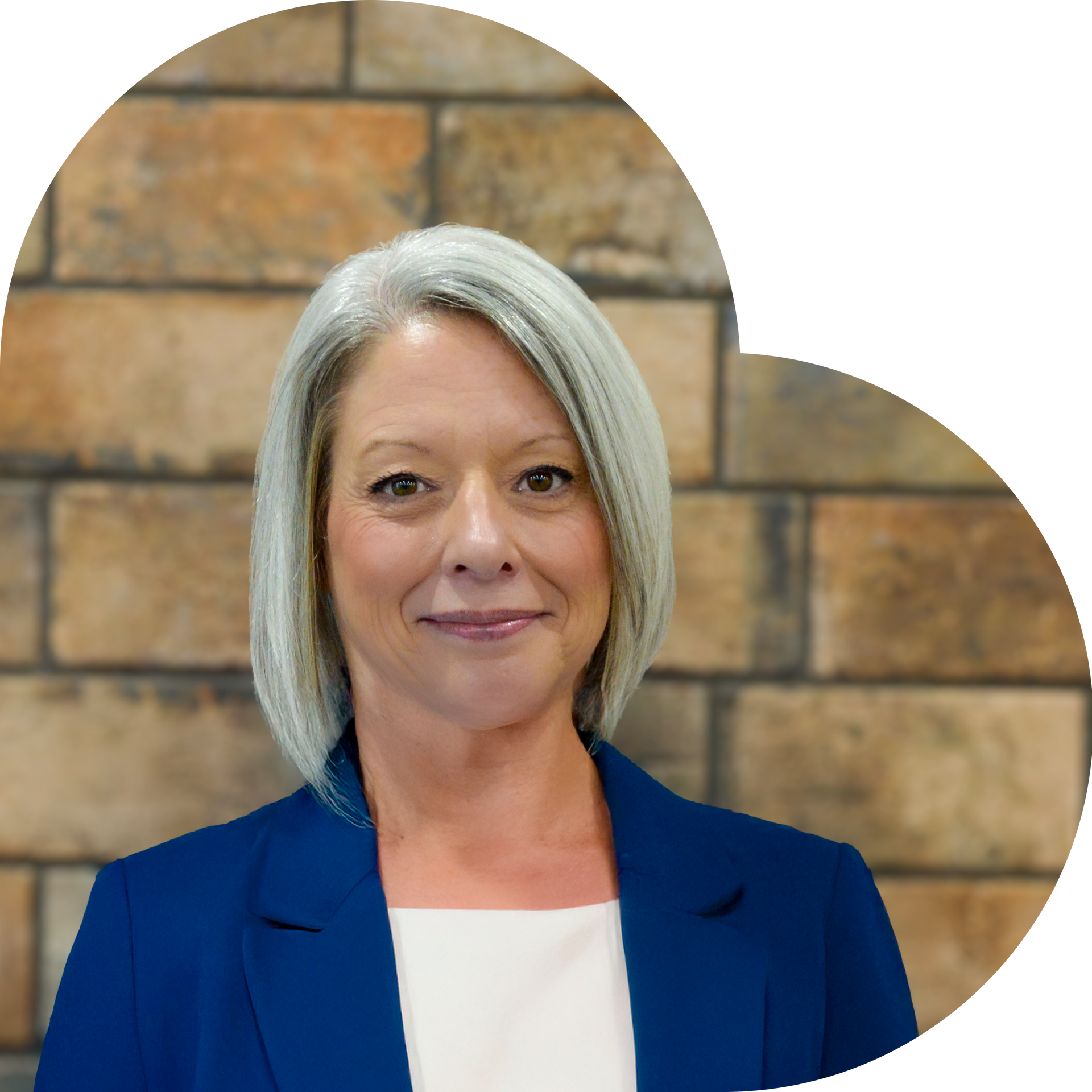 Woman in a blue blazer smiles, set against a brick heart-shaped background.