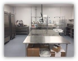 Commercial kitchen with stainless steel appliances and prep tables; food storage boxes visible.