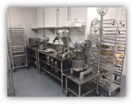 Commercial kitchen with stainless steel mixers, racks, and prep areas.
