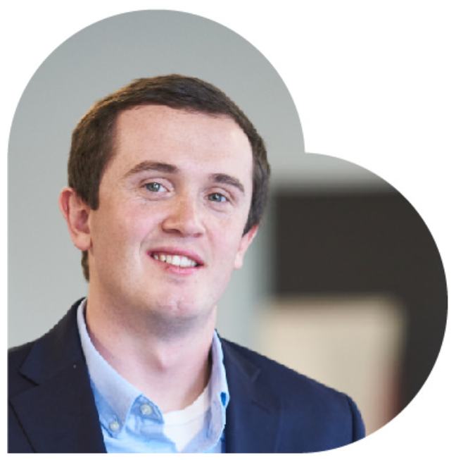 Young man in a blue blazer smiles. He's in a well-lit room with a blurred background.
