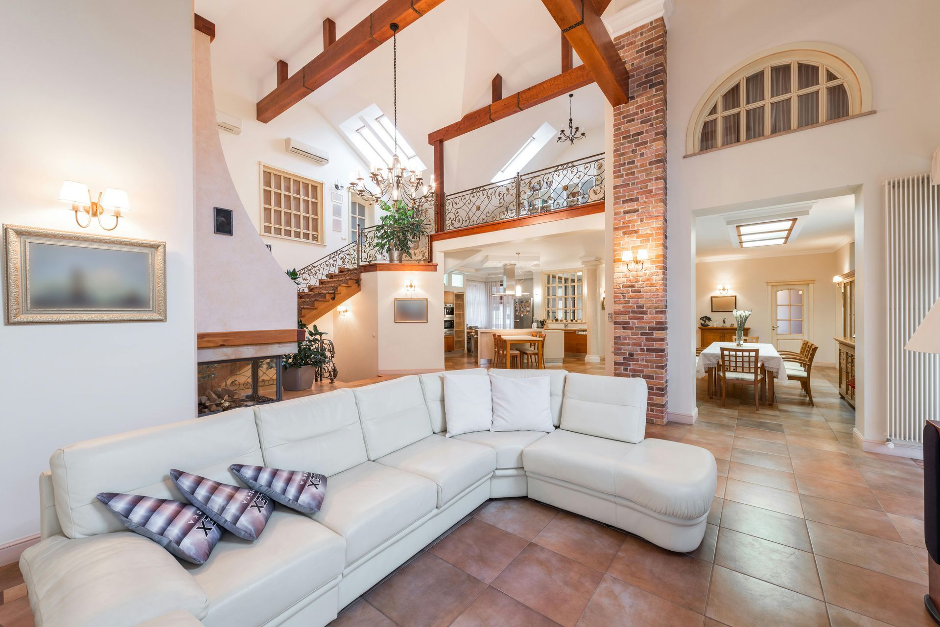 Bright open living room with white sectional sofa, exposed beams, stone fireplace, and arched doorway