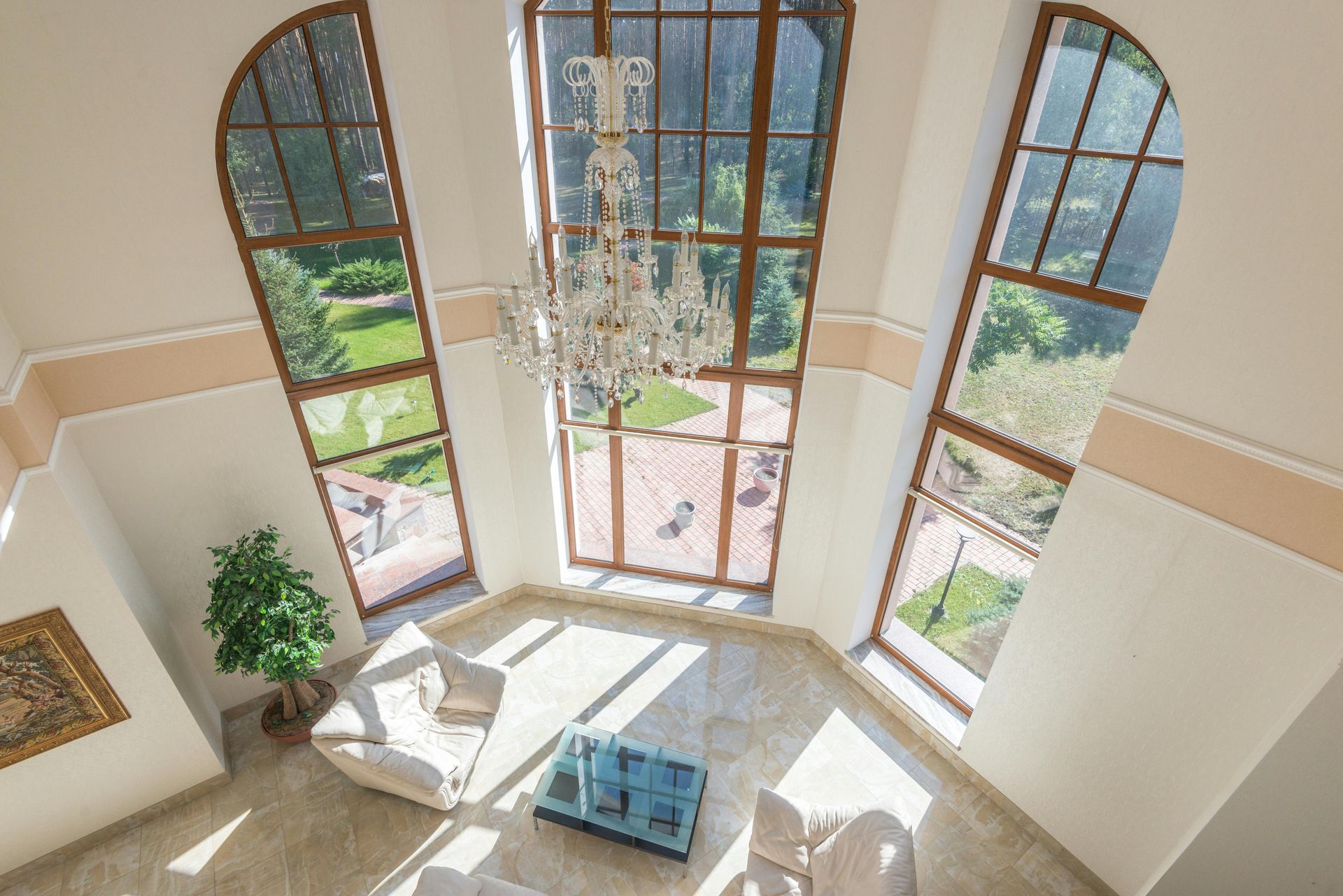 Bright two-story foyer with arched windows, chandelier, white furniture, and a potted plant.
