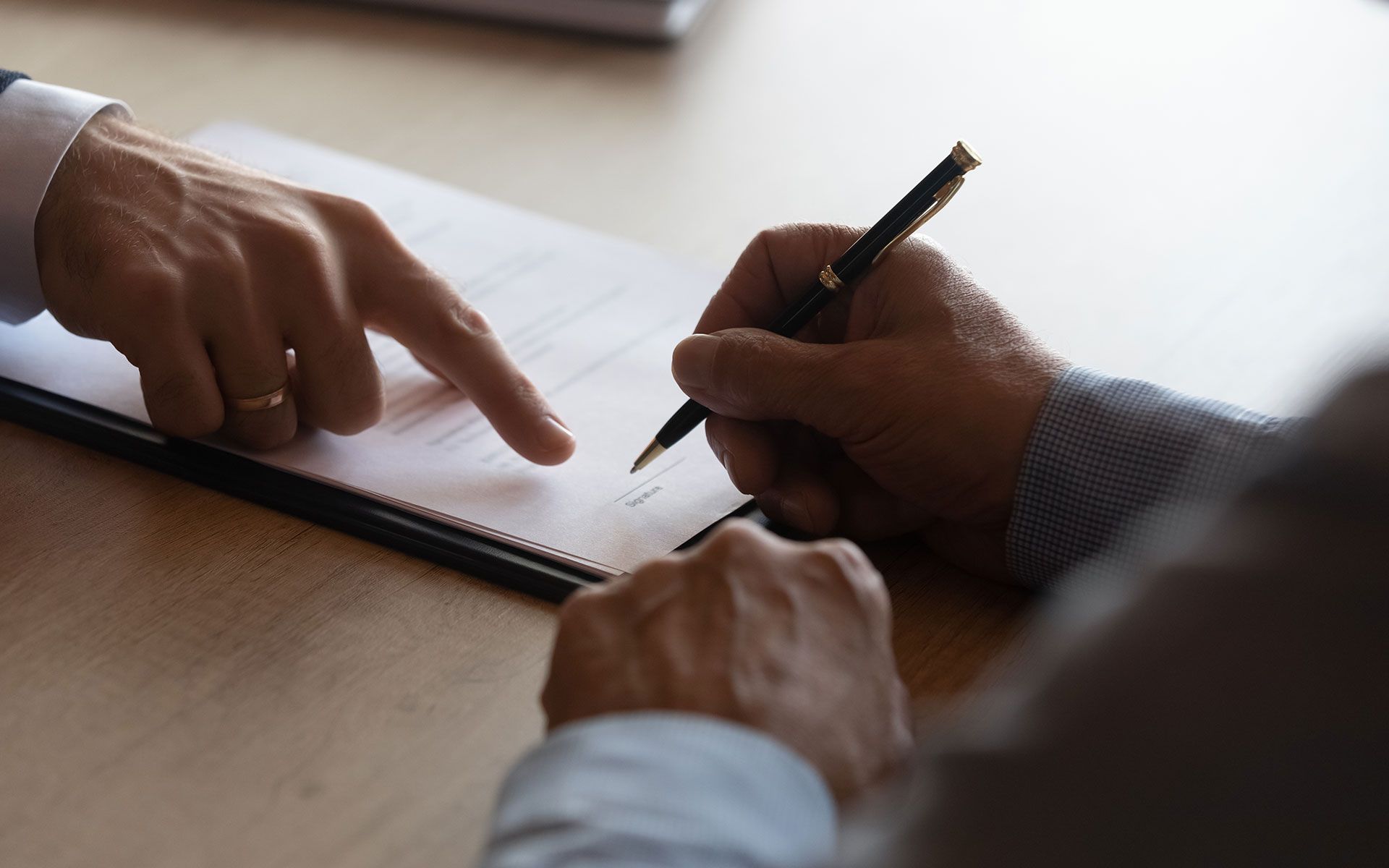 A man is signing a document with a pen and pointing at it.