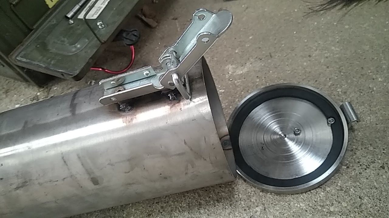 Un réservoir en acier inoxydable avec le couvercle ouvert est posé sur le sol.