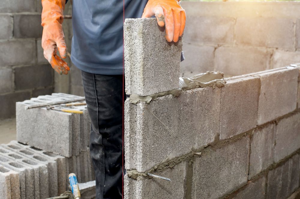 Construction Worker in Orange Gloves Laying a Cinder Block with Mortar — DGW Wholesale Timber & Hardware in Rutherford, NSW