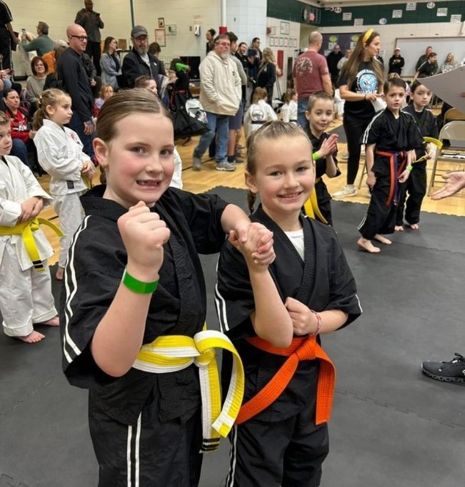 People practicing jiu-jitsu on mats, wearing gis in blue, black, and gray. Active grappling, gym setting.