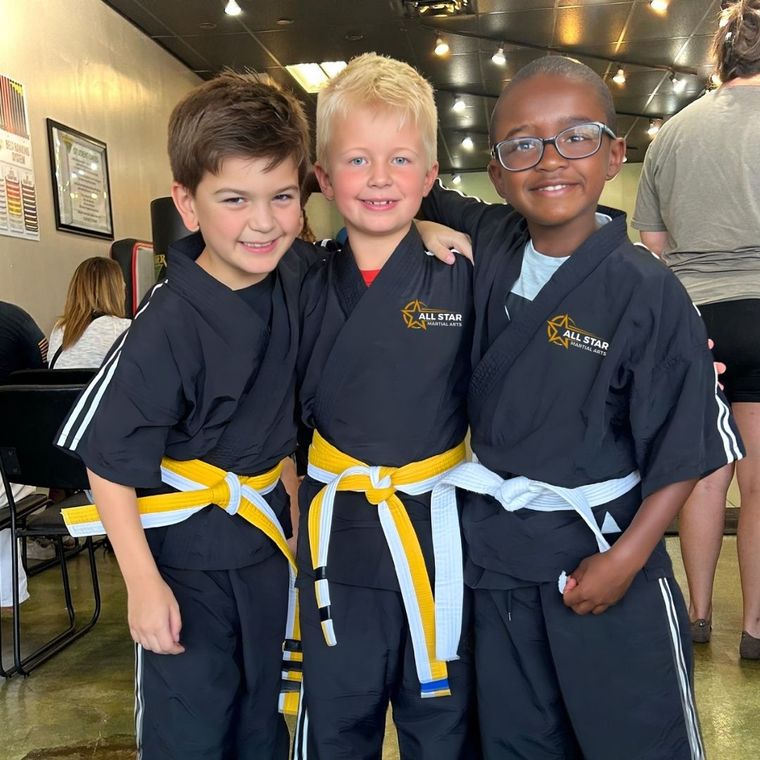 Family in Jiu-Jitsu gis poses. Indoors, blue mats, a smiling woman in the middle, around a seated man with a beard.
