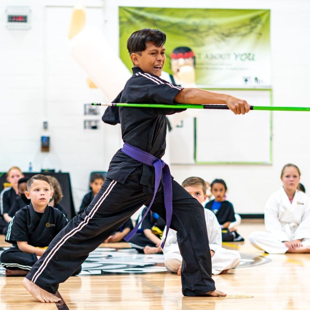 Two people grappling on a mat, one in a black gi, the other in a rash guard, legs entangled.