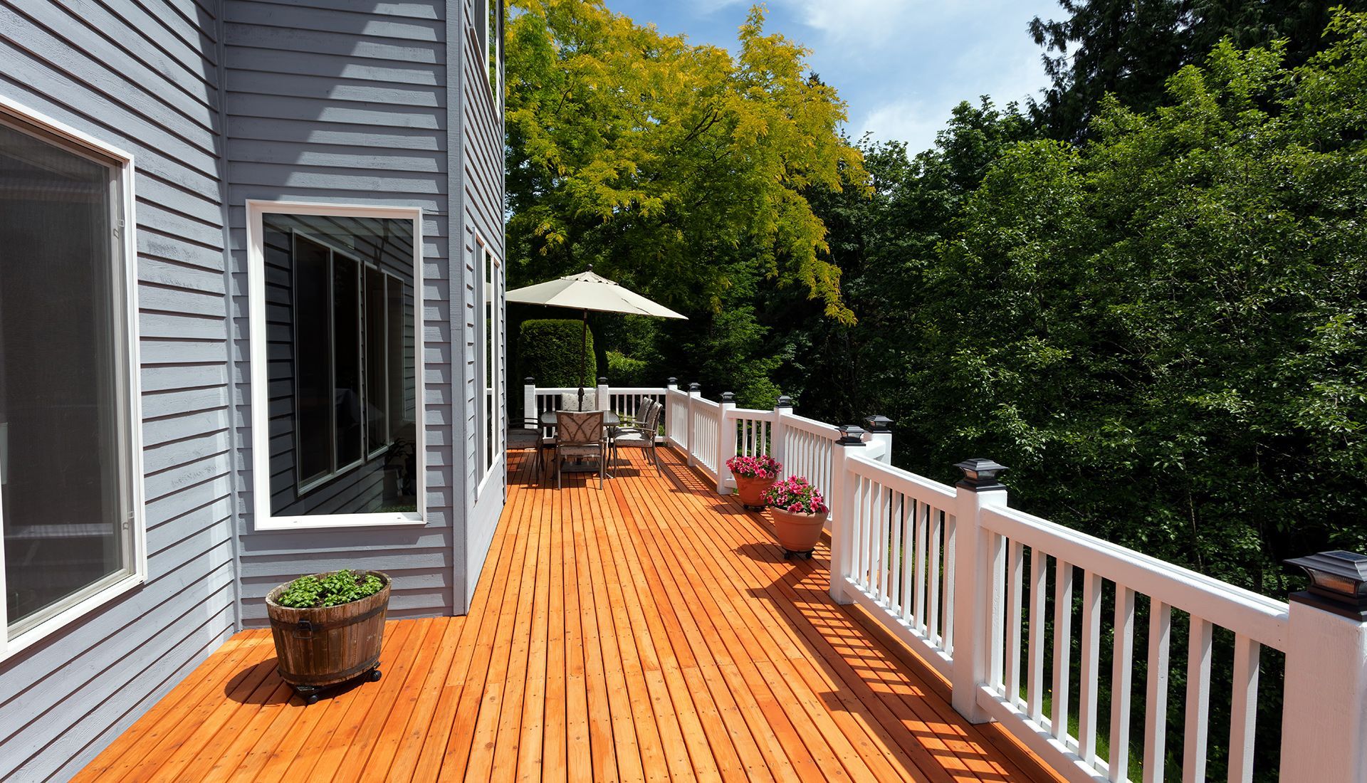A large wooden deck with a white railing surrounded by trees