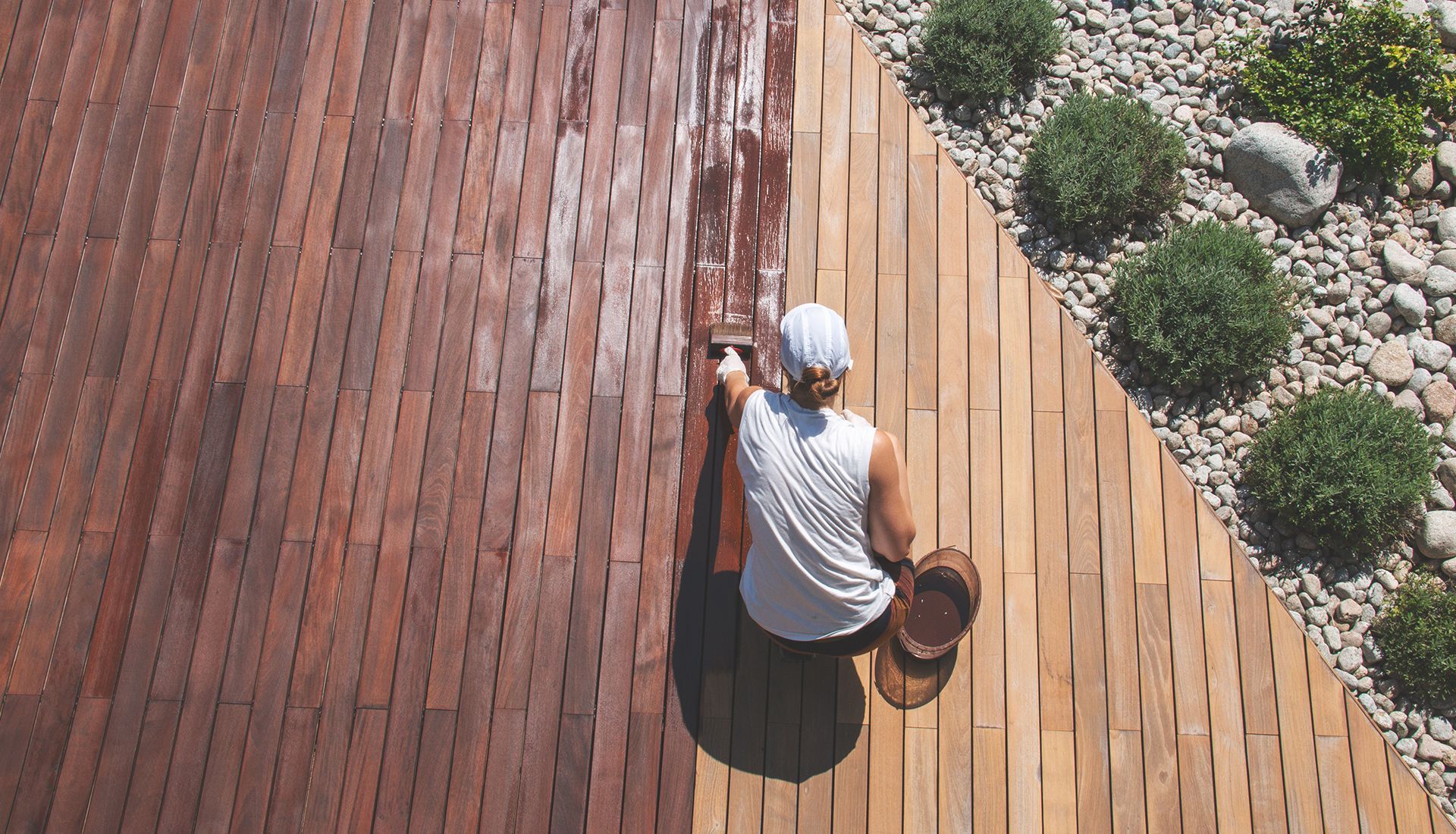 A man is painting a wooden deck with a brush.
