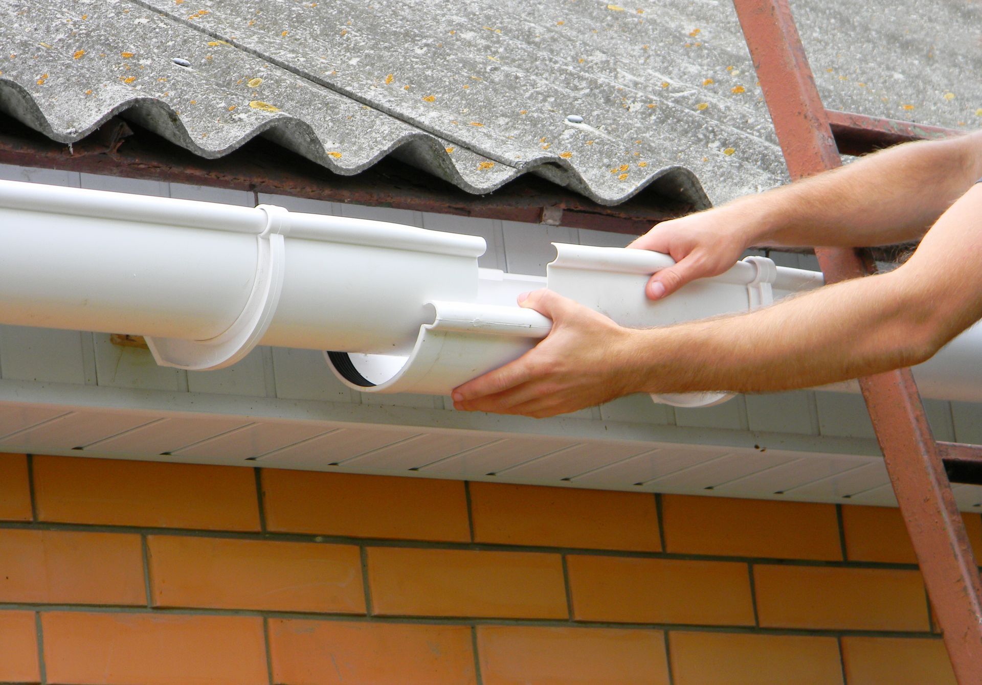A man is installing a gutter on the roof of a house.