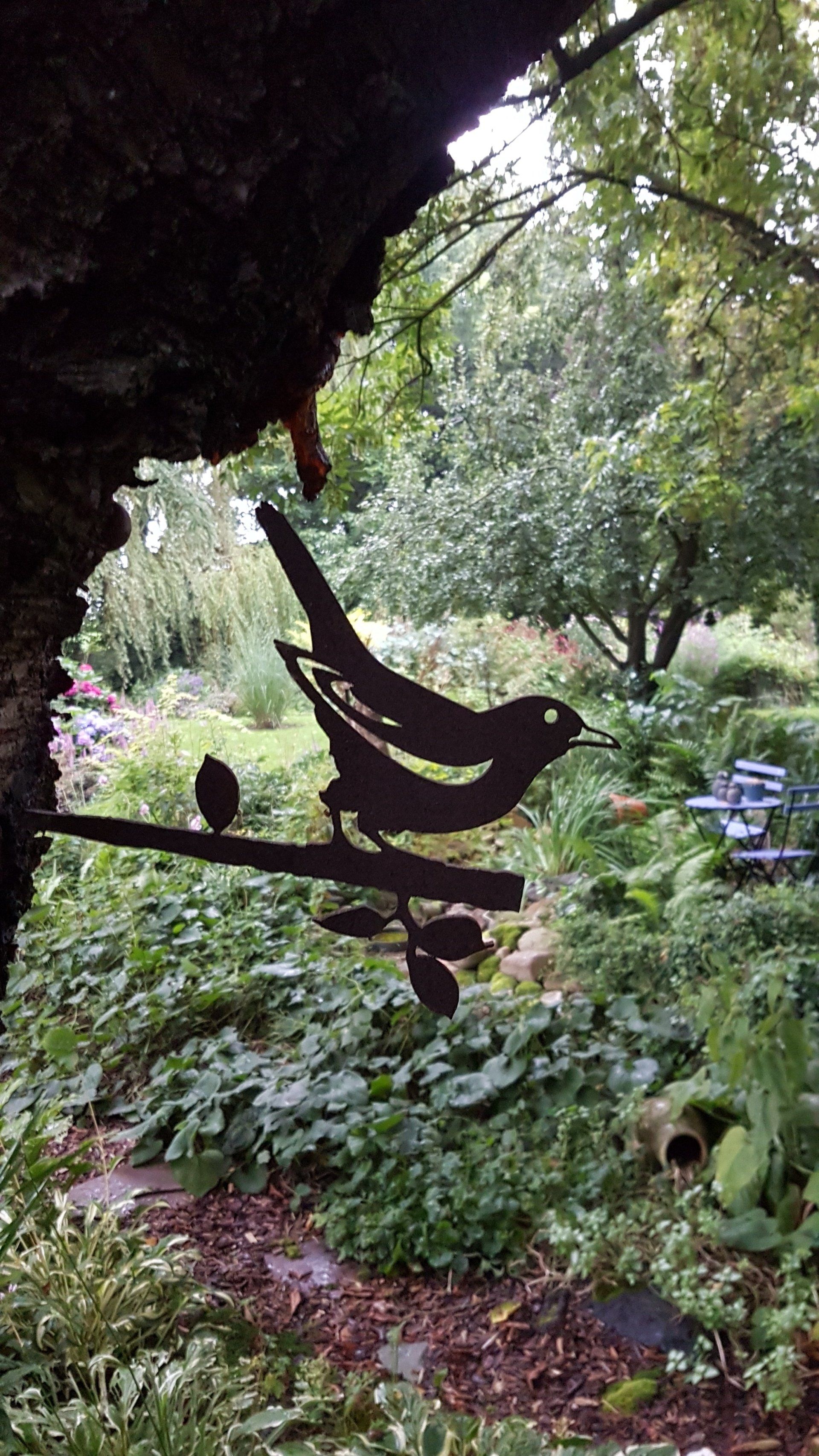 Een silhouet van een vogel die op een tak in een tuin zit.