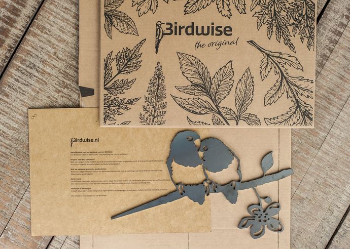 Lasergesneden vogelkunst op een achtergrond van kraftpapier. De kunst toont twee vogels op een tak en een bloemenversiering.