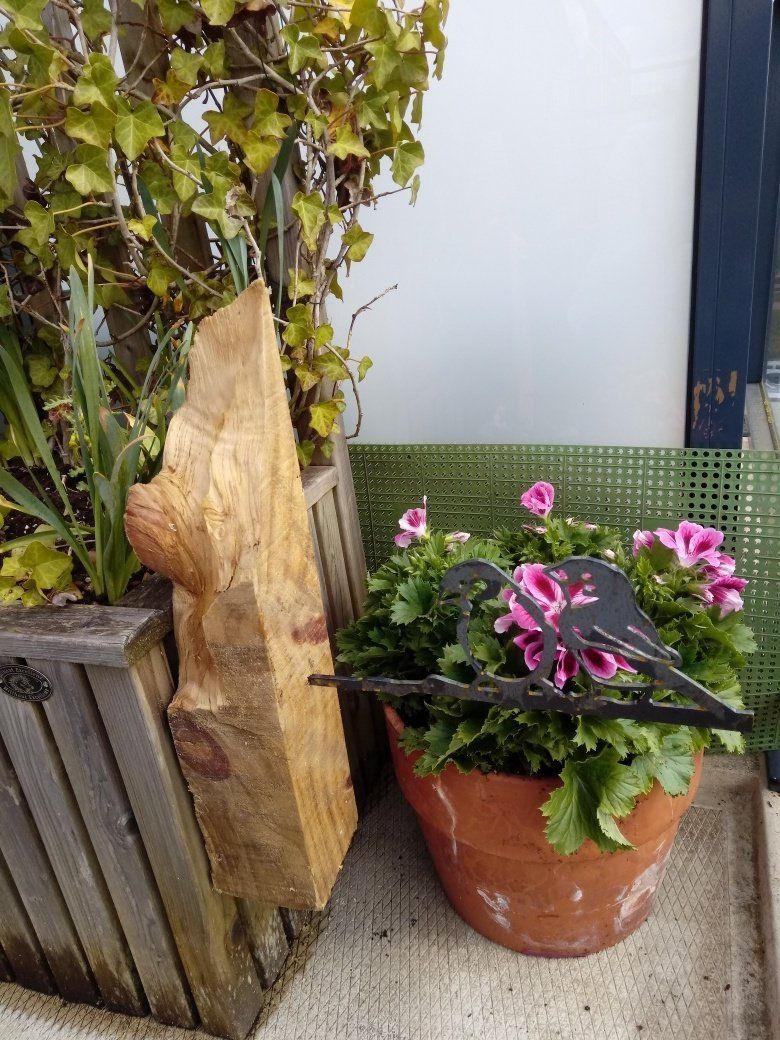 Een standbeeld van een vogel zit naast een potplant met roze bloemen.