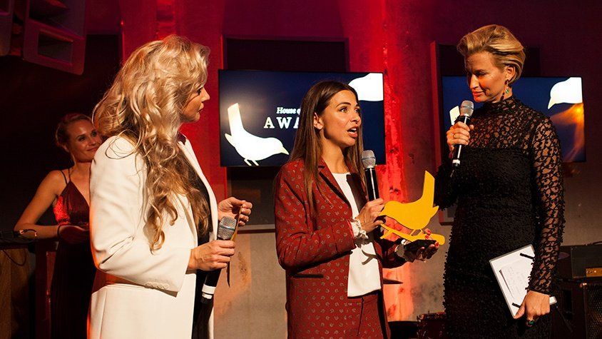 Drie vrouwen staan ​​op een podium met microfoons in hun handen.