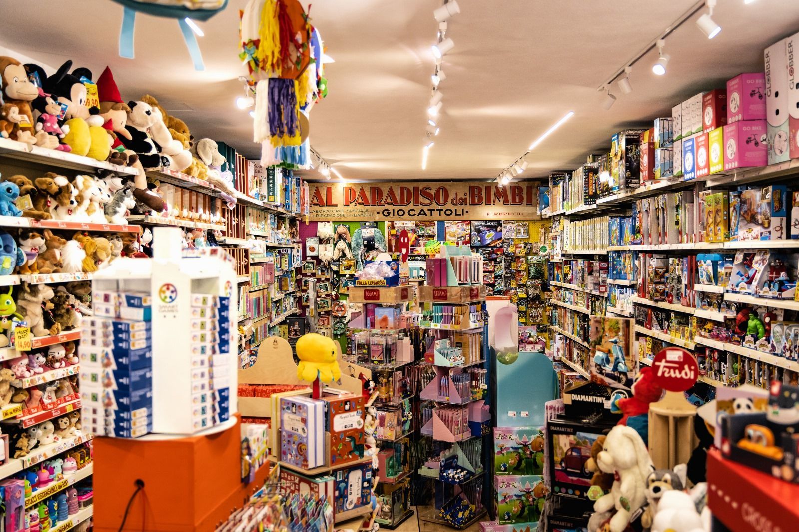 Interno di un negozio di giocattoli pieno di scaffali, animali di peluche e vari prodotti colorati.