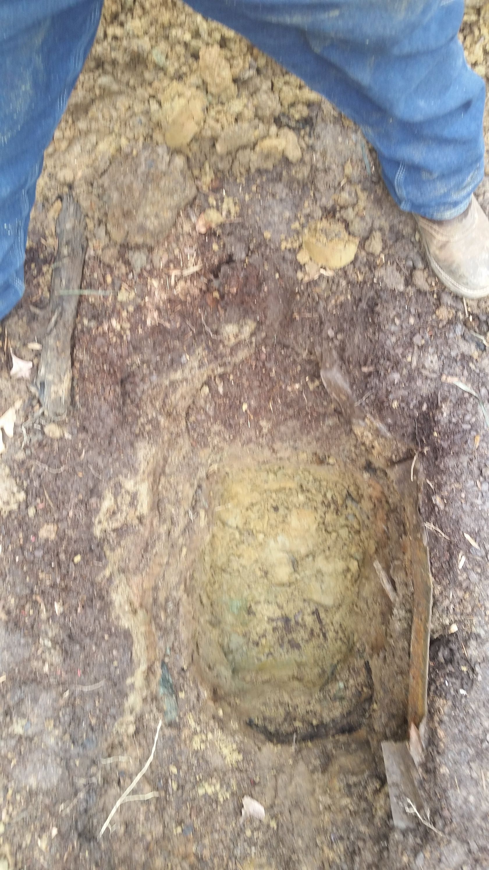 Person near a hole in the ground with greenish soil. Wooden pieces are visible.