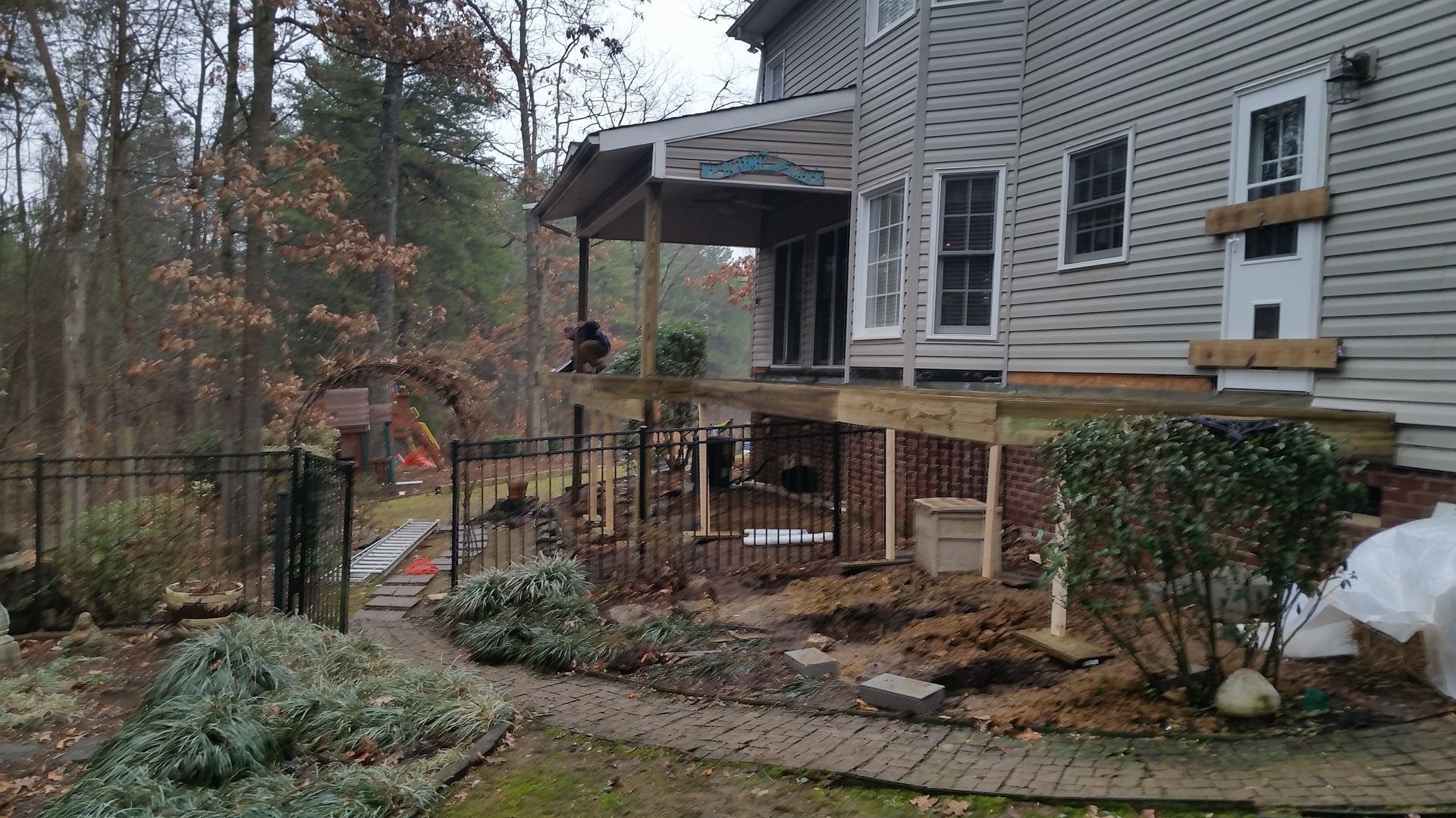 Exterior of a house undergoing construction with a partially built deck and surrounding landscaping.