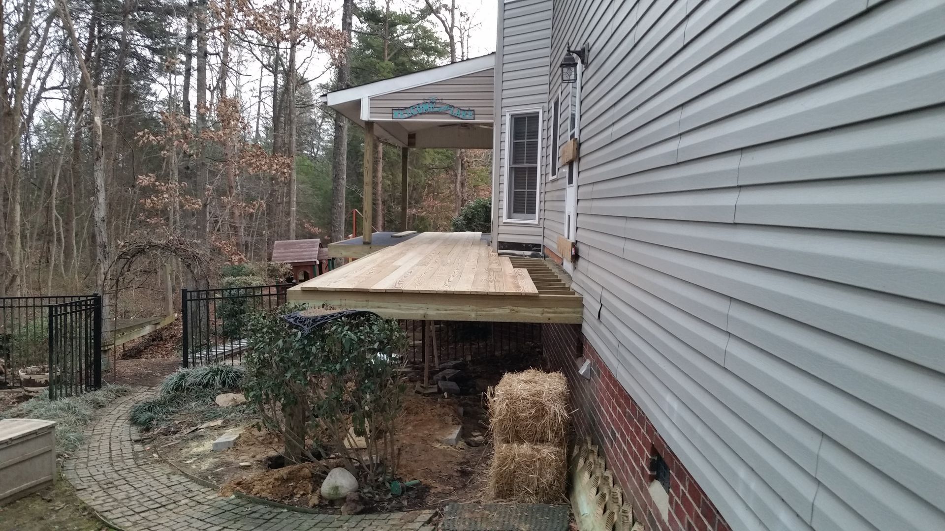 Wooden deck attached to a house with gray siding; pathway and forest in the background.