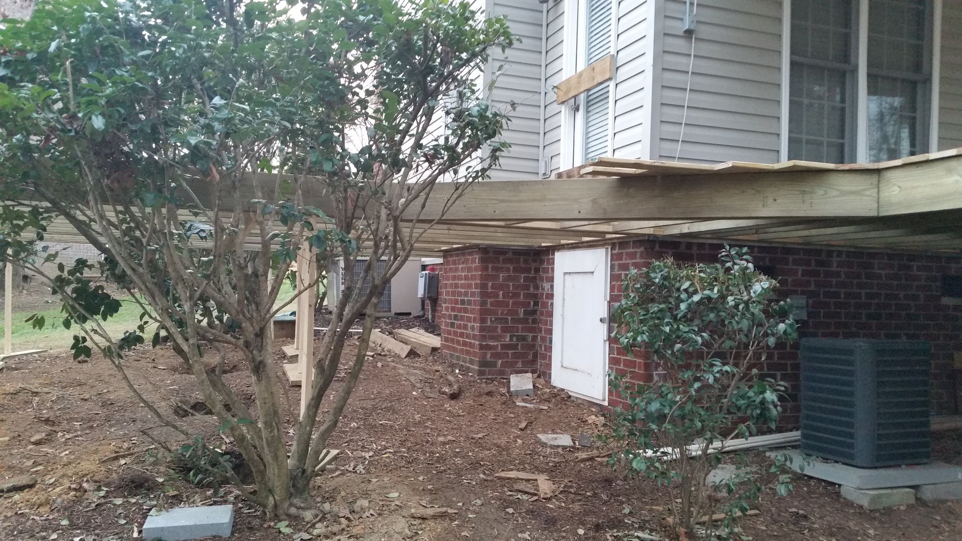 House under construction with exposed brick foundation, white door, and deck supports.