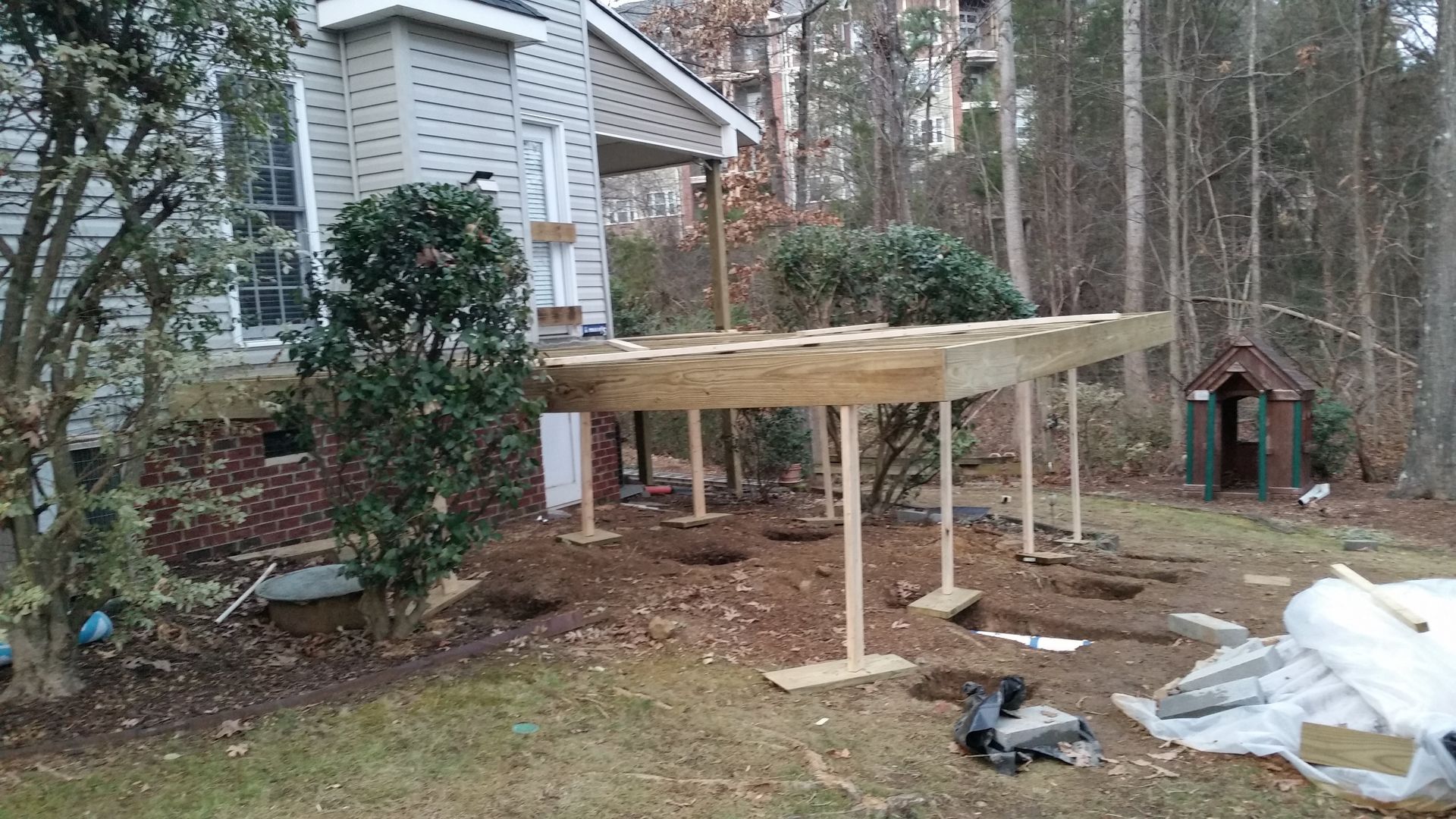 A partially built wooden deck in a backyard, with support posts and a playhouse in the distance.
