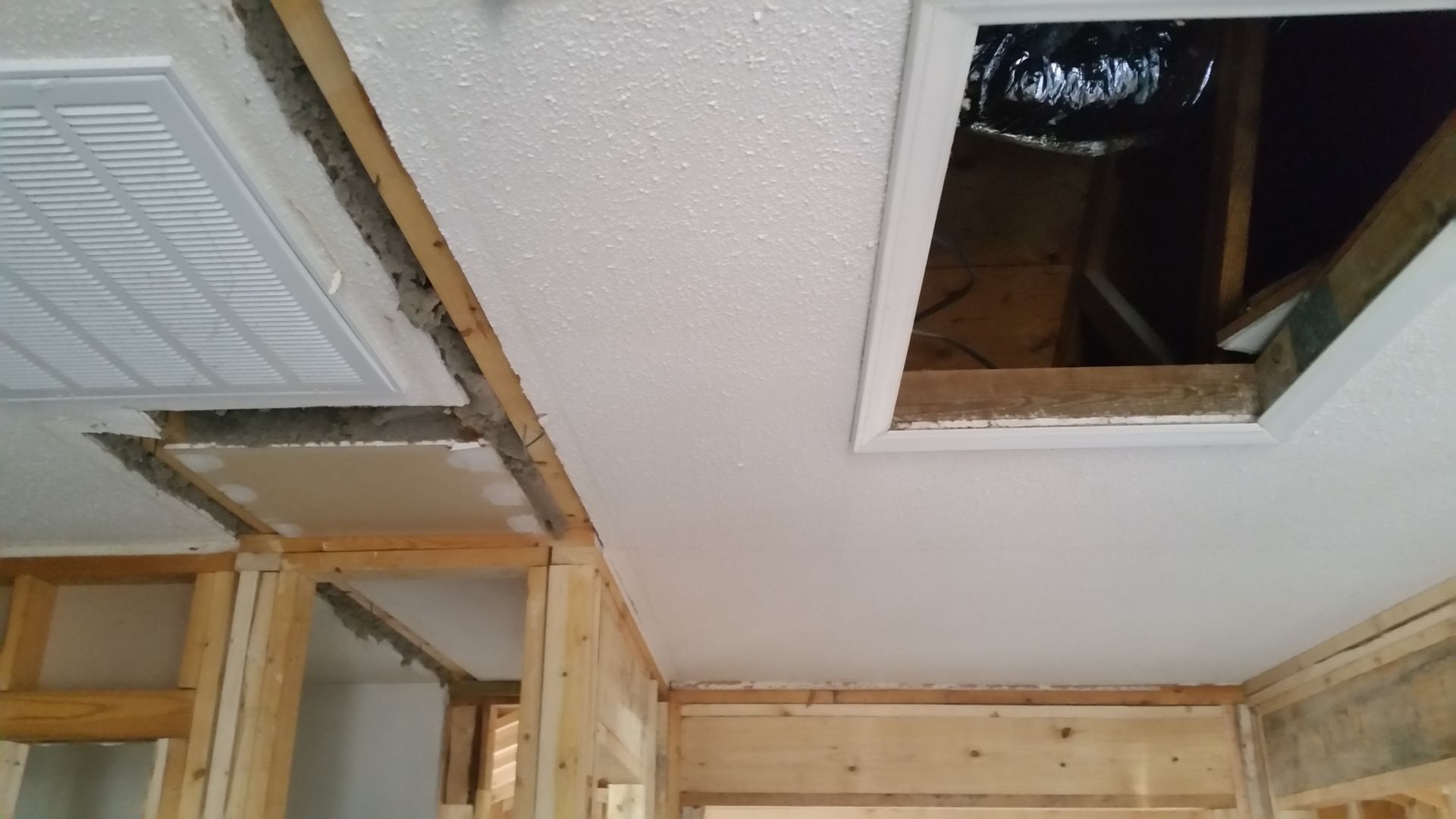 Ceiling under construction: hole in textured white ceiling with exposed framing and ductwork.