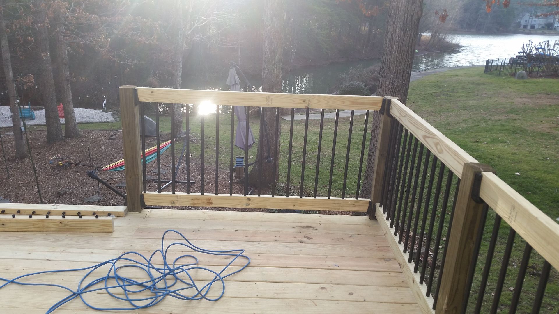 Deck with black railings, wooden posts, and lake view. Sun shining.