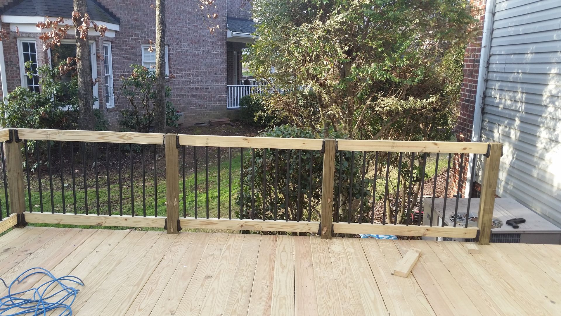 Wooden deck with black railing and a backyard view, under a sunny sky.