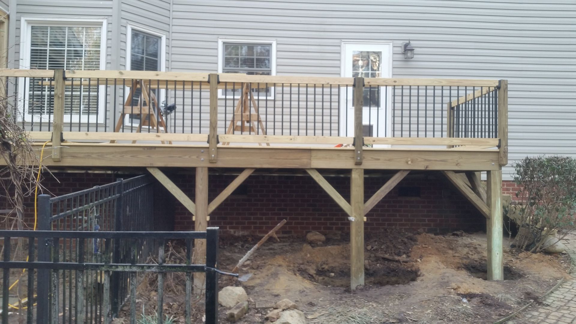 Wooden deck attached to a house with black railing and support beams.