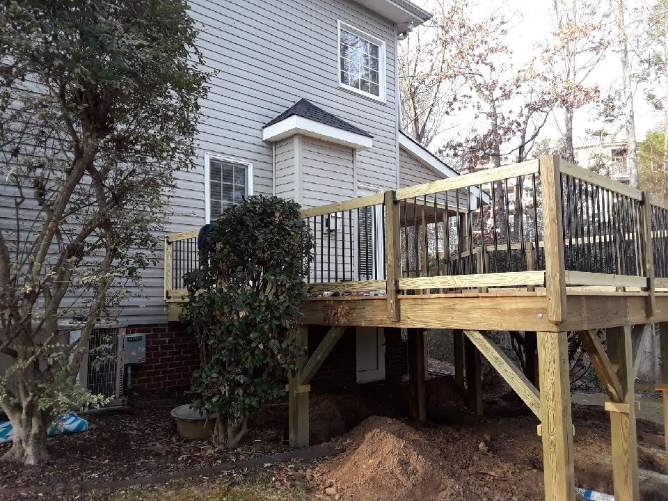 Wooden deck attached to a gray house, featuring black railings, visible support beams, and a surrounding yard.