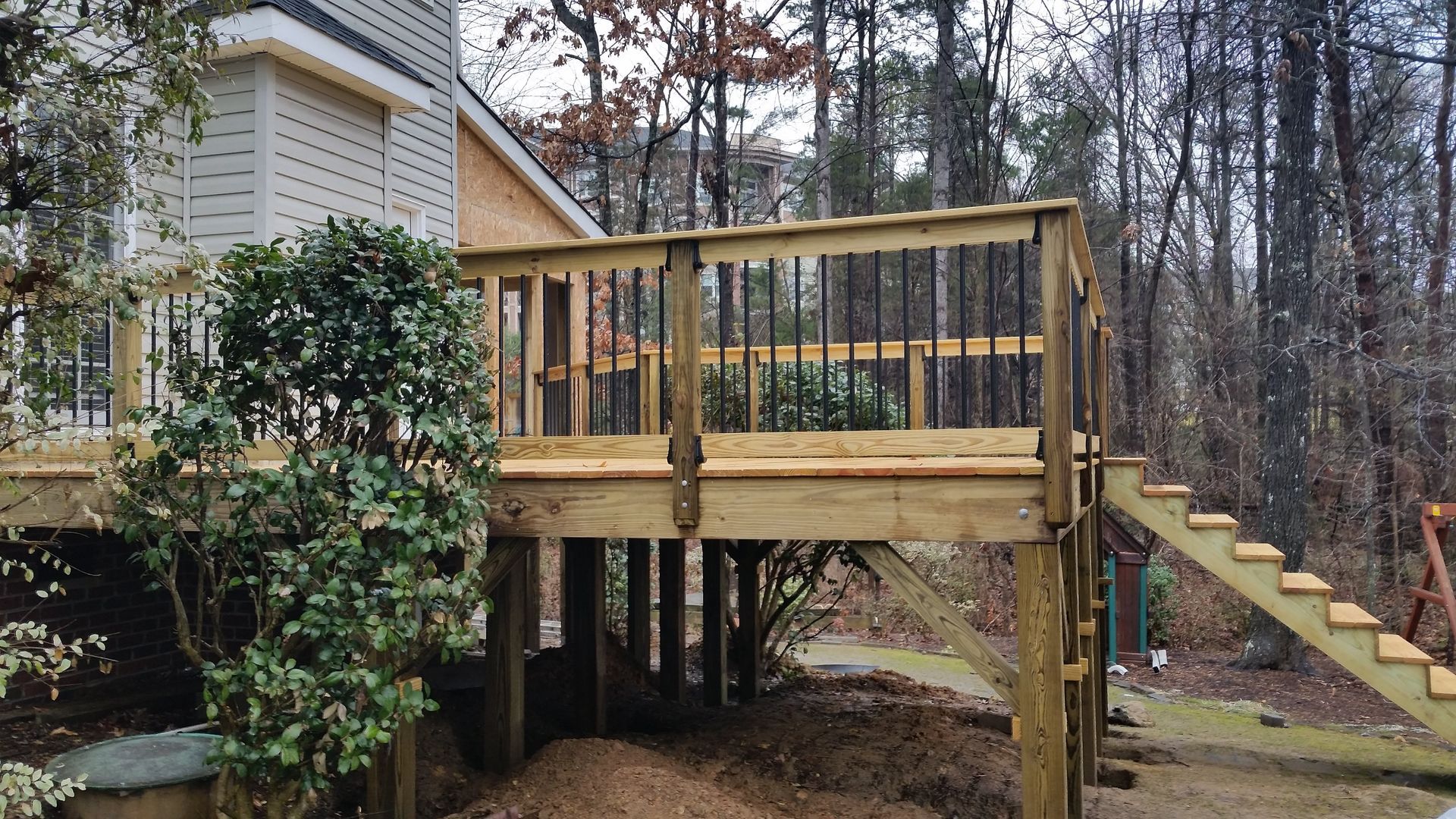 Wooden deck with stairs, built on posts, surrounded by trees.