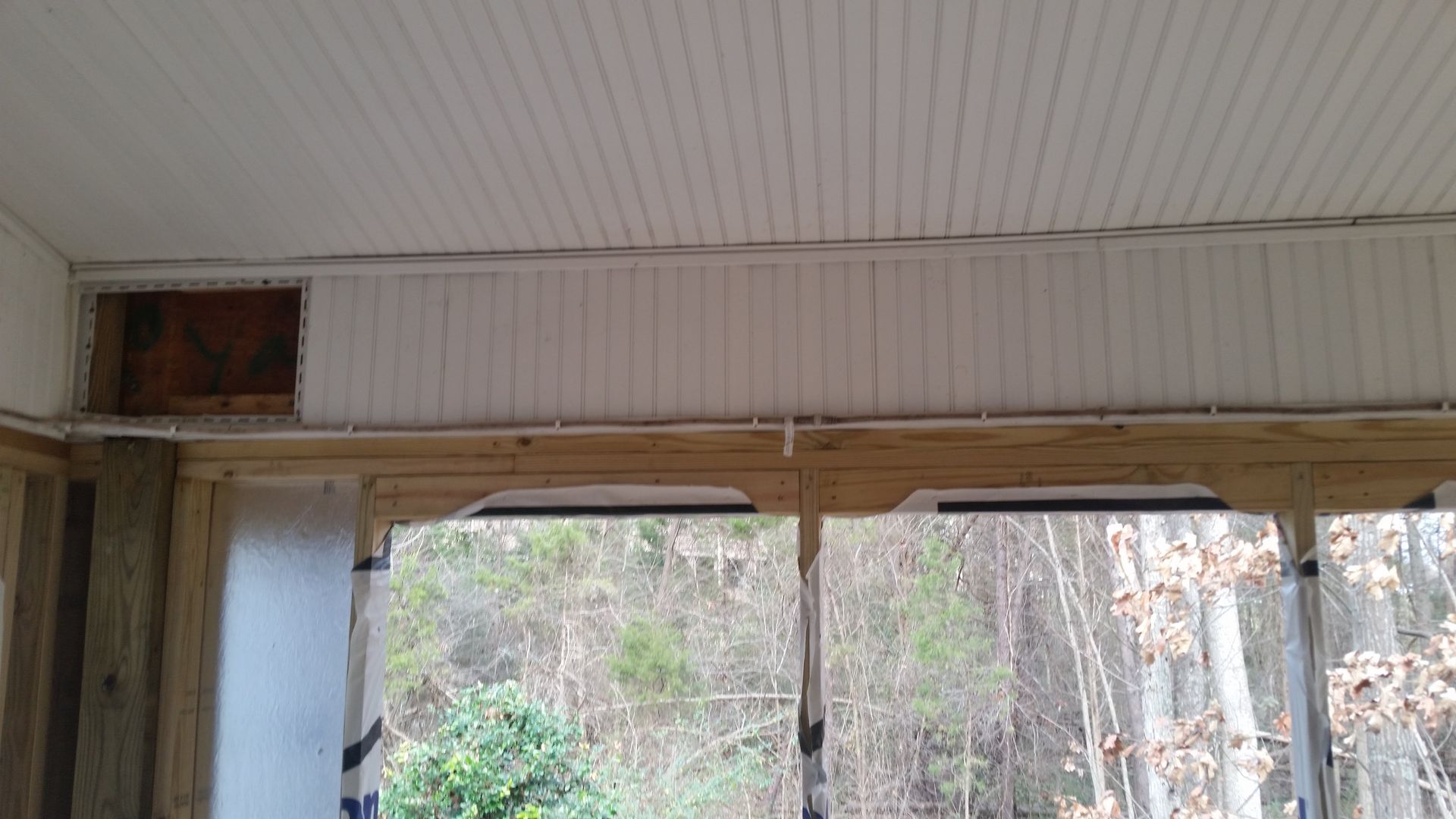 White paneled porch ceiling and walls, with view of trees and foliage.
