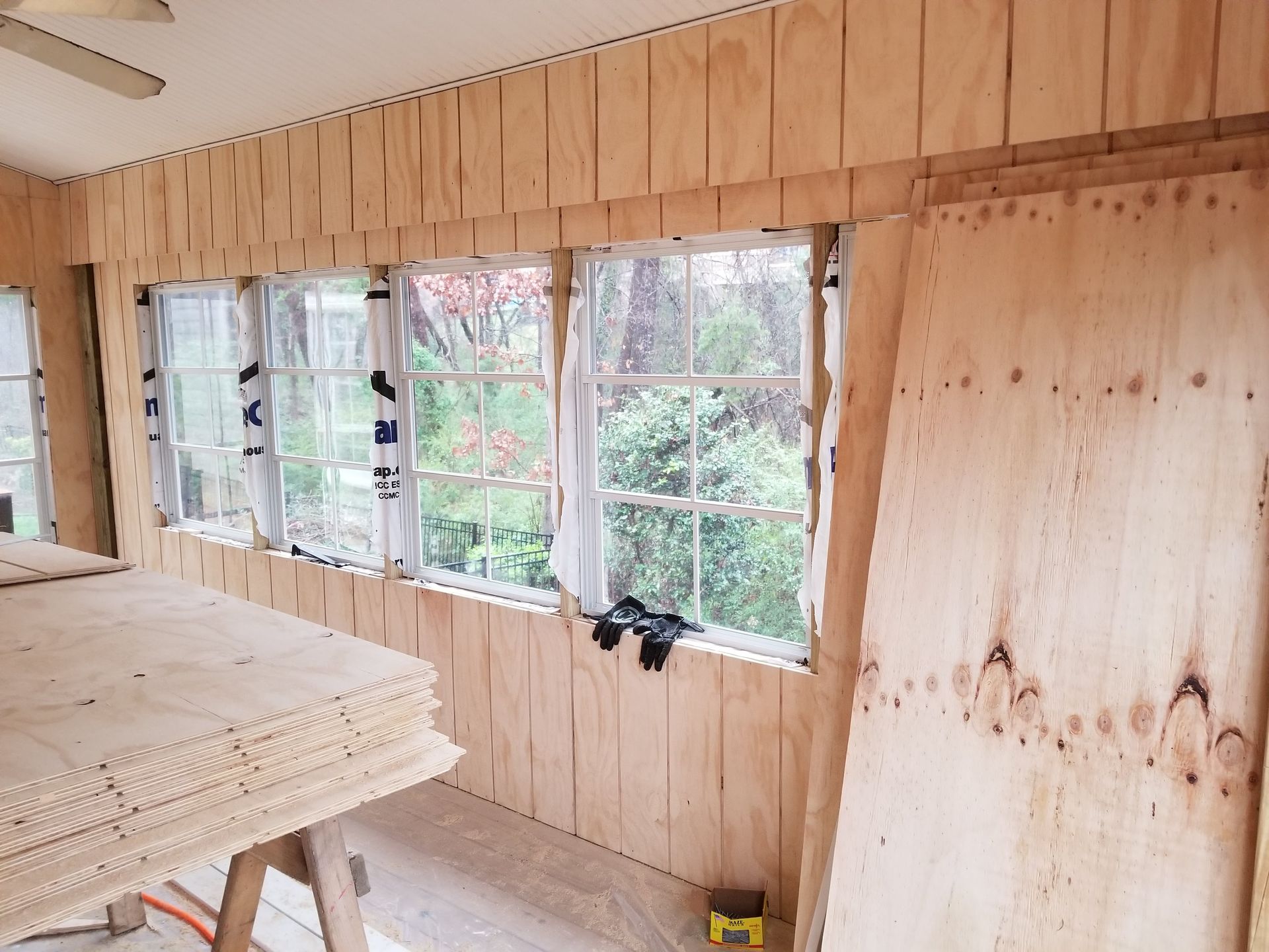 Interior with unfinished plywood walls, windows, and stacks of plywood.
