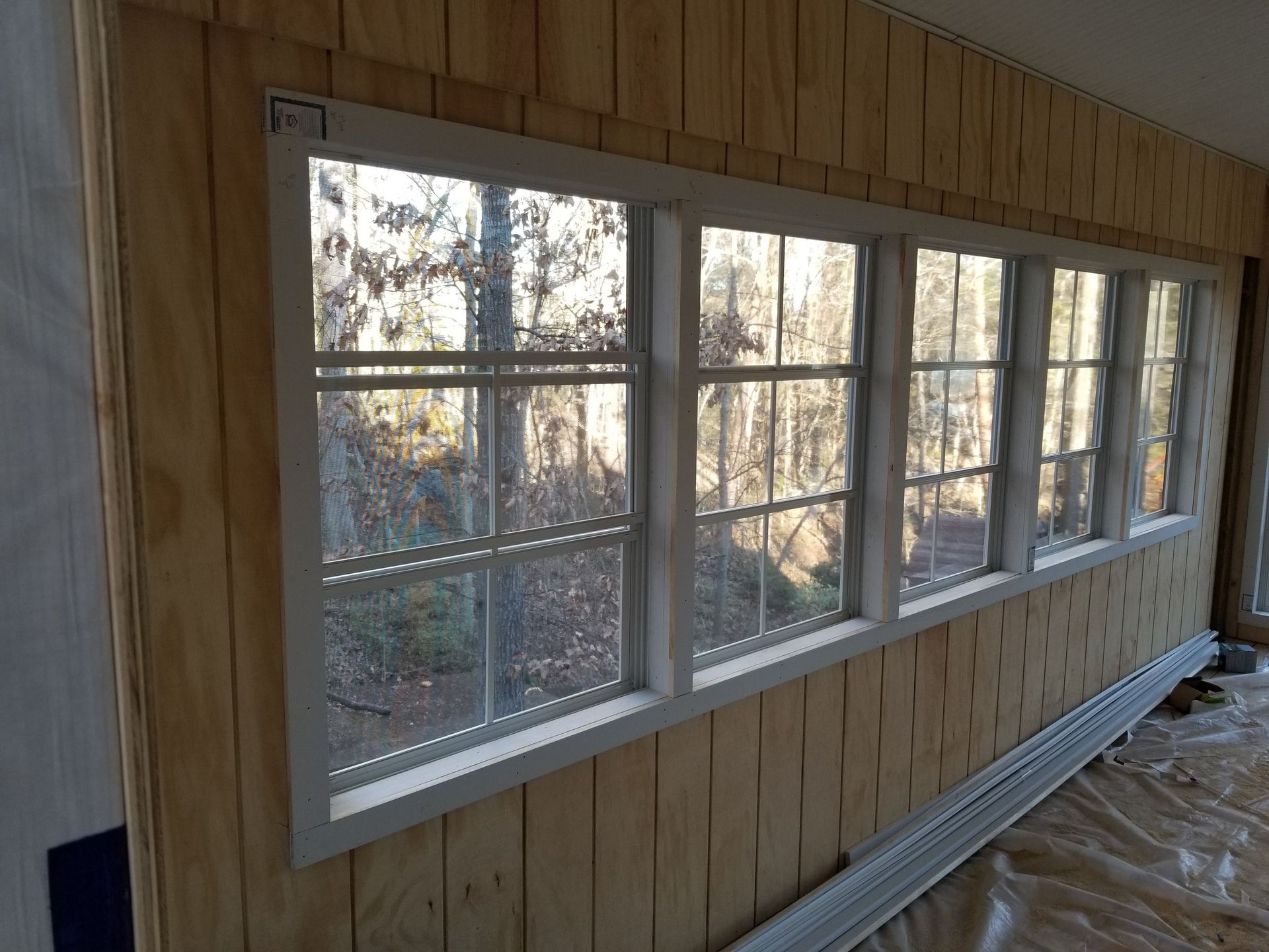 Six-pane window in a room with light wood paneling, looking out to trees and sunlight.