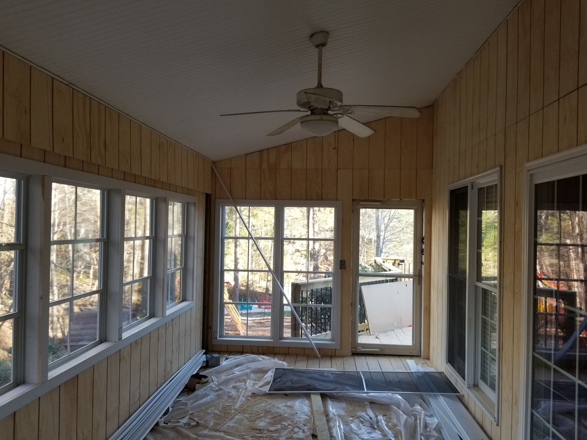 Sunroom with light wood paneling, windows, and ceiling fan. Protective covering on the floor.