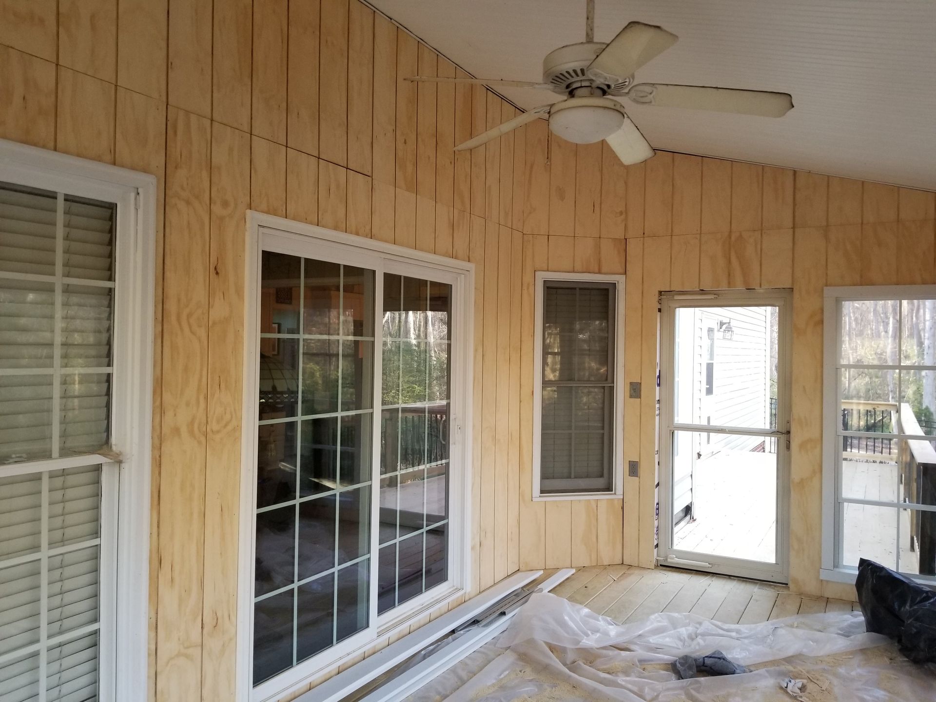 Sunroom interior with unfinished wood paneling, sliding door, windows, and ceiling fan.